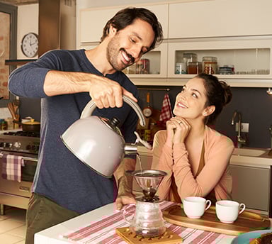 Homem servindo uma xícara de café Café Apricot na xícara de café de sua esposa na mesa da cozinha.